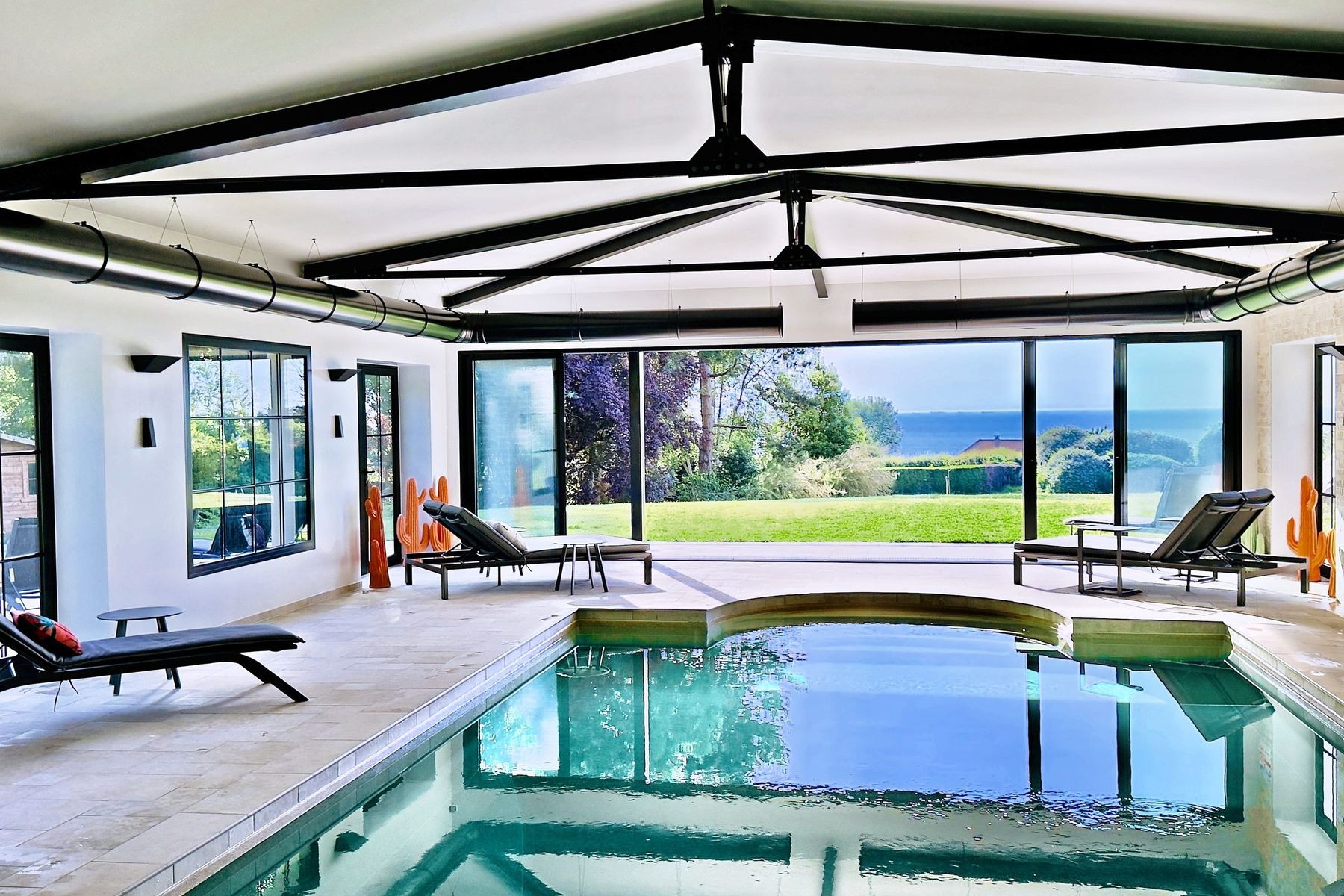 The orangery's large glass door open onto the park lawn and the sea, seen from the edge of the indoor pool