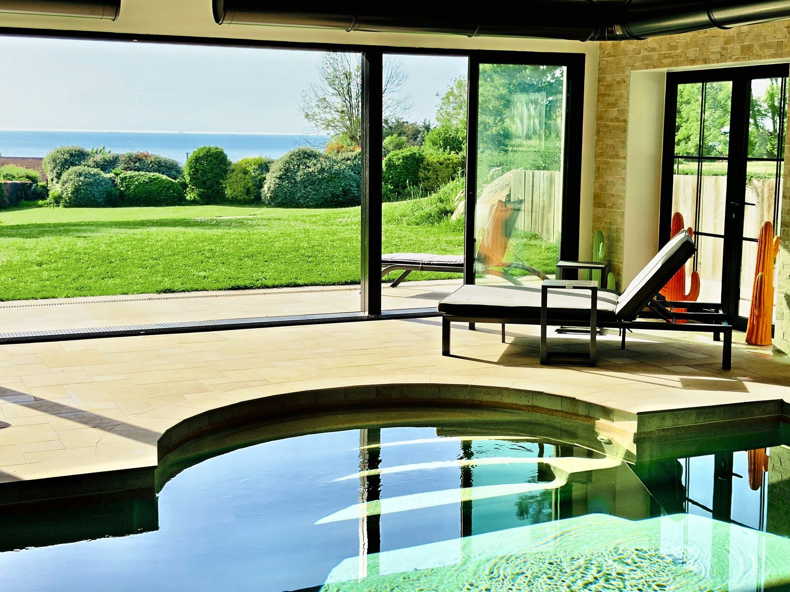 The indoor pool steps in the sun, turquoise water, the lawn and the sea beyond the glass door